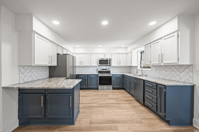 kitchen with stainless steel appliances, blue cabinets, a sink, and white cabinetry