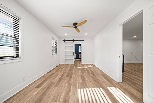 empty room with light wood finished floors, a barn door, baseboards, ceiling fan, and recessed lighting