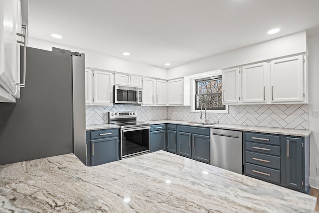 kitchen featuring a sink, white cabinets, appliances with stainless steel finishes, light stone countertops, and tasteful backsplash