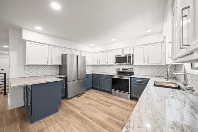 kitchen featuring blue cabinets, appliances with stainless steel finishes, light stone countertops, and white cabinets