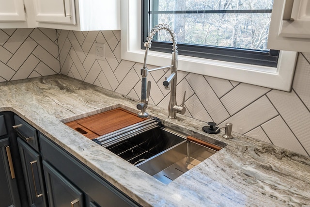 interior space featuring light stone counters, backsplash, a sink, and white cabinetry