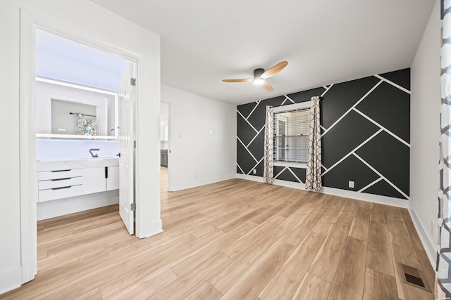 interior space with ceiling fan, an accent wall, visible vents, baseboards, and light wood-type flooring