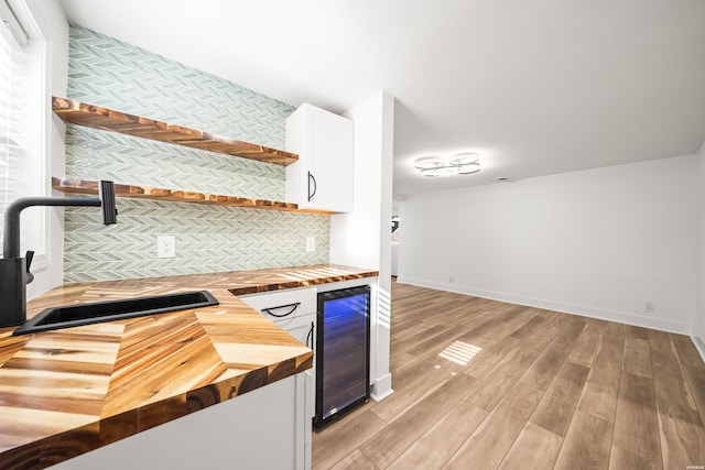 kitchen with beverage cooler, light wood-style flooring, wood counters, open shelves, and a sink