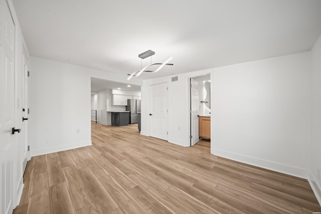 unfurnished living room featuring visible vents, light wood-style flooring, and baseboards