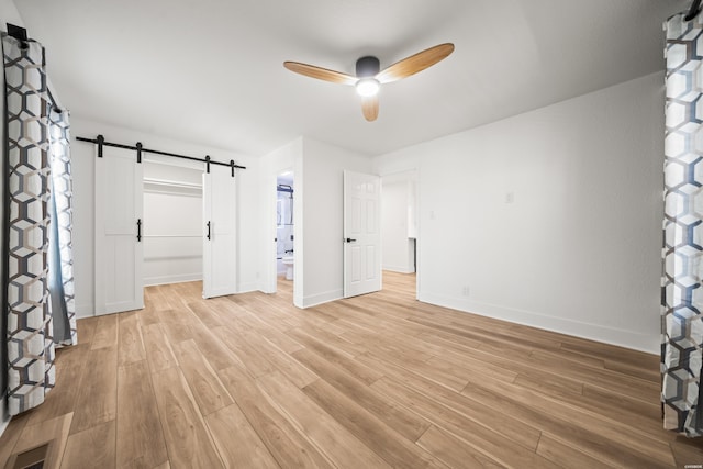 unfurnished bedroom featuring visible vents, a spacious closet, a barn door, light wood-style floors, and baseboards