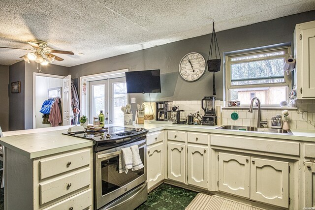 kitchen featuring a peninsula, a sink, light countertops, stainless steel electric range oven, and decorative light fixtures