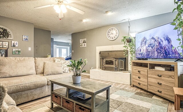 living room with light wood-style floors, a wood stove, ceiling fan, and a textured ceiling