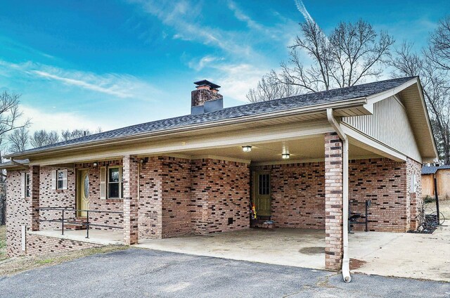 exterior space featuring aphalt driveway, brick siding, a chimney, and a carport