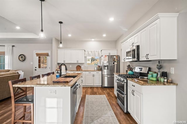 kitchen with stainless steel appliances, a sink, white cabinetry, an island with sink, and dark stone countertops