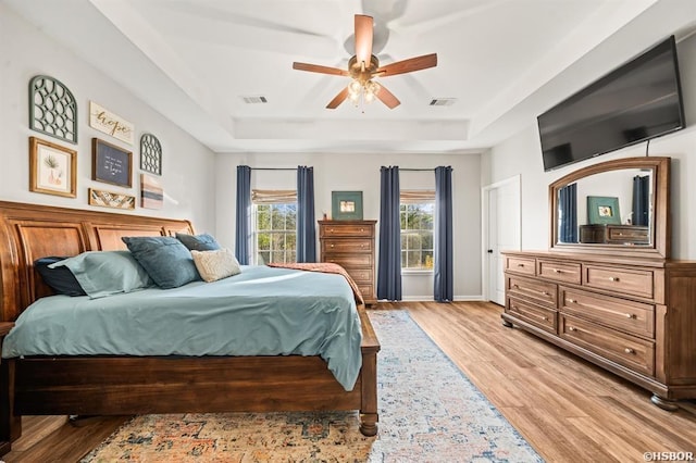 bedroom featuring a tray ceiling, a ceiling fan, visible vents, and light wood-style floors