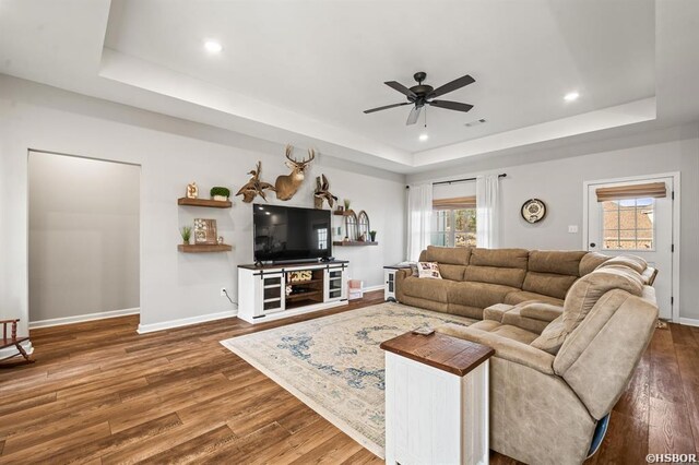 living area featuring recessed lighting, wood finished floors, a ceiling fan, baseboards, and a raised ceiling