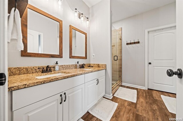 bathroom with double vanity, a shower stall, a sink, and wood finished floors