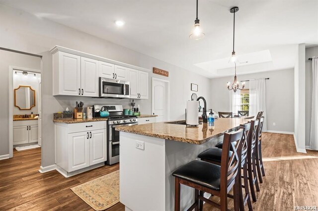 kitchen with stone counters, pendant lighting, a center island with sink, appliances with stainless steel finishes, and white cabinetry