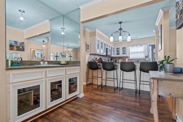 bar featuring stainless steel microwave, dark wood-style flooring, crown molding, a chandelier, and a sink