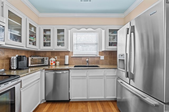 kitchen with stainless steel appliances, stone countertops, glass insert cabinets, white cabinets, and a sink