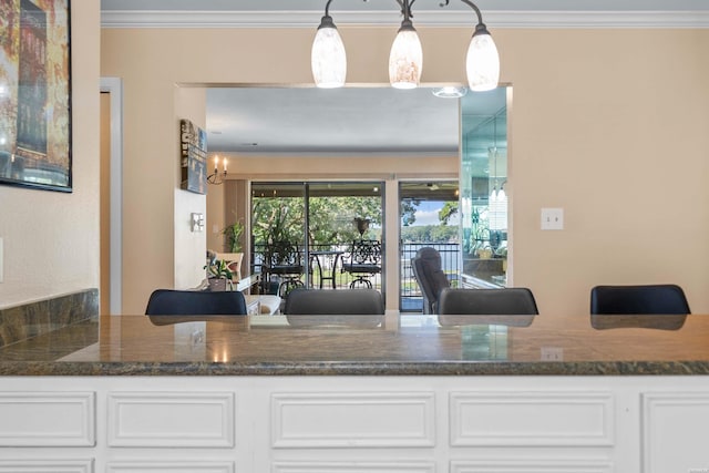 interior space with white cabinetry, pendant lighting, crown molding, and dark stone counters