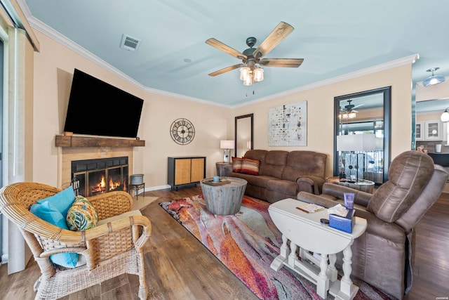 living area with wood finished floors, visible vents, baseboards, a glass covered fireplace, and crown molding