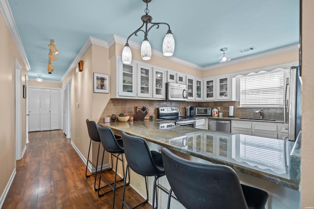 kitchen with white cabinets, glass insert cabinets, appliances with stainless steel finishes, a peninsula, and a sink