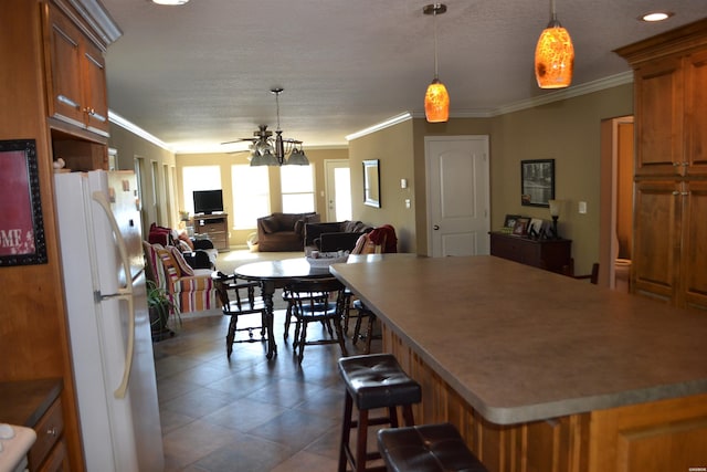 kitchen featuring brown cabinetry, a breakfast bar area, open floor plan, freestanding refrigerator, and crown molding