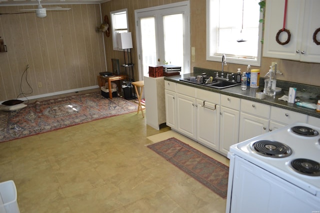 kitchen featuring light floors, white range with electric cooktop, dark countertops, white cabinets, and a sink