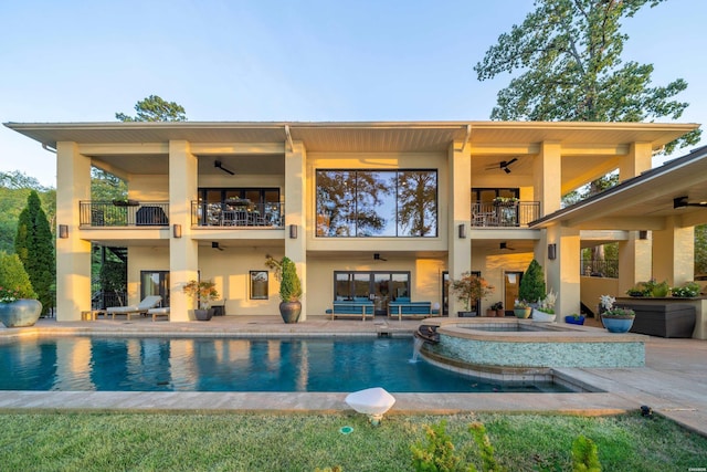 back of house with a balcony, an outdoor pool, a ceiling fan, and an in ground hot tub