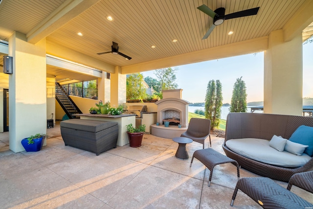 view of patio with a water view, an outdoor living space with a fireplace, an outdoor kitchen, a ceiling fan, and stairs