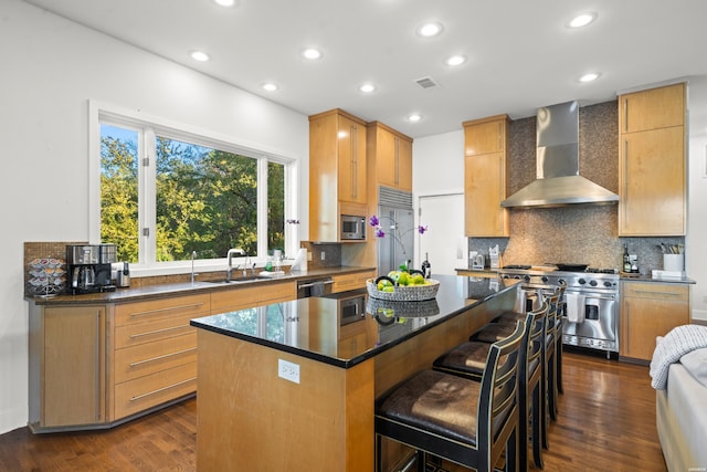 kitchen featuring dark countertops, a kitchen island, wall chimney range hood, a sink, and built in appliances