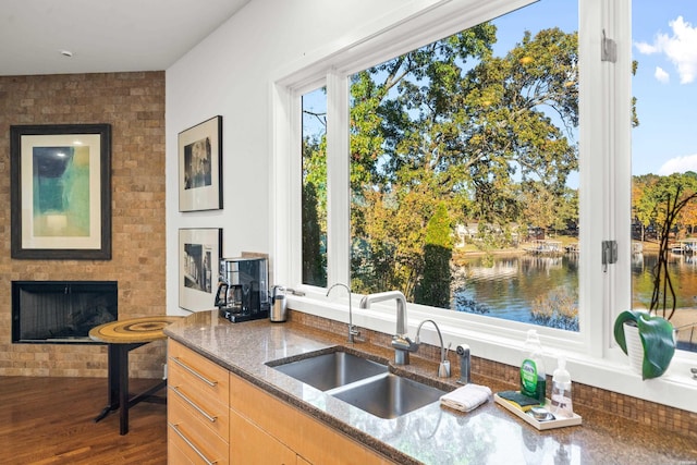 kitchen with dark stone countertops, a fireplace, a water view, and a sink