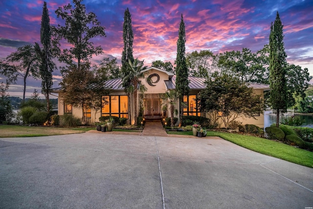 view of front of house with stucco siding, concrete driveway, a standing seam roof, metal roof, and a front lawn