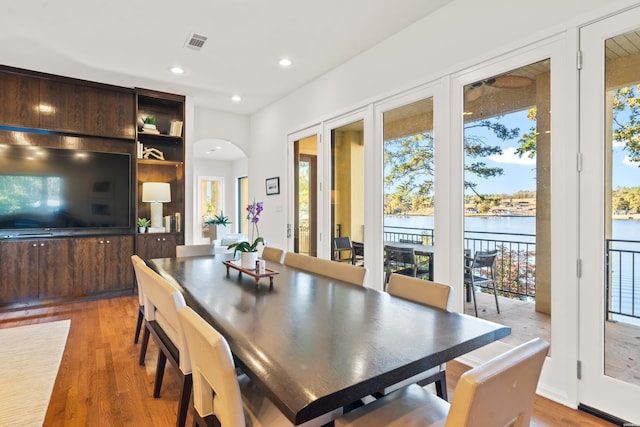 dining area featuring a water view, visible vents, arched walkways, and wood finished floors