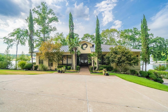 view of front facade with metal roof, a standing seam roof, a front yard, and stucco siding