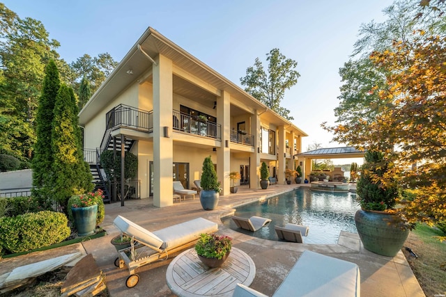 rear view of house with stairs, a patio area, a balcony, and stucco siding