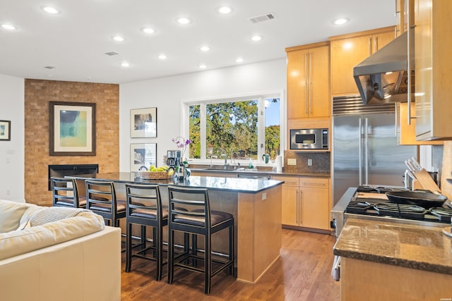 kitchen with a kitchen breakfast bar, a center island, built in appliances, a fireplace, and exhaust hood