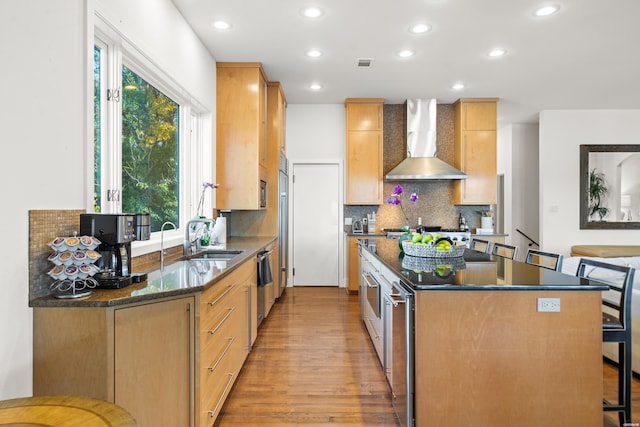 kitchen with visible vents, light wood-style flooring, backsplash, wall chimney range hood, and a sink