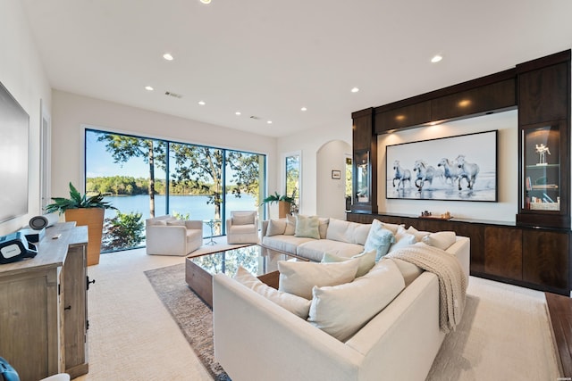 living room with visible vents, arched walkways, light colored carpet, a water view, and recessed lighting