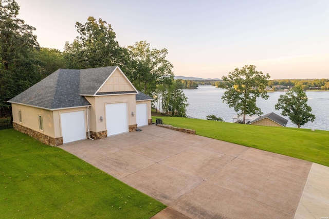 garage at dusk with a garage, a yard, and a water view