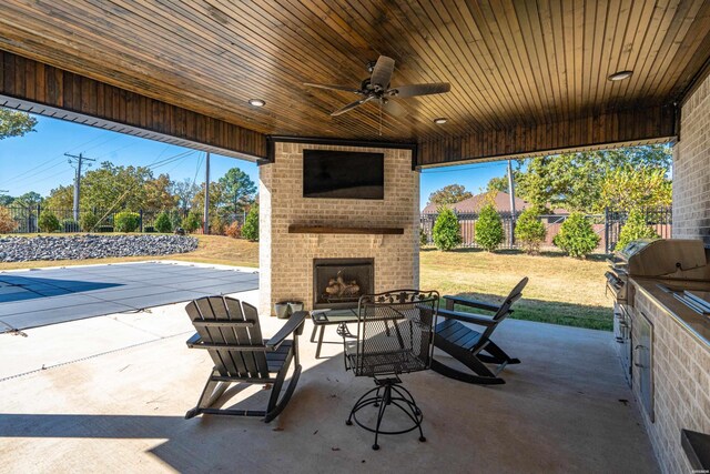 view of patio / terrace featuring an outdoor brick fireplace, a fenced backyard, grilling area, and a ceiling fan