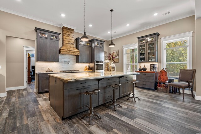 kitchen featuring glass insert cabinets, decorative light fixtures, a center island with sink, and dark brown cabinets