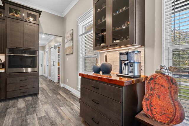 kitchen featuring dark brown cabinetry, a barn door, glass insert cabinets, ornamental molding, and oven