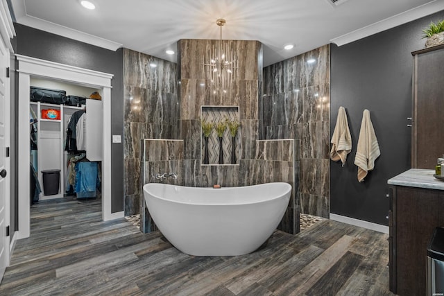 full bathroom featuring a walk in closet, a freestanding tub, vanity, and wood finished floors