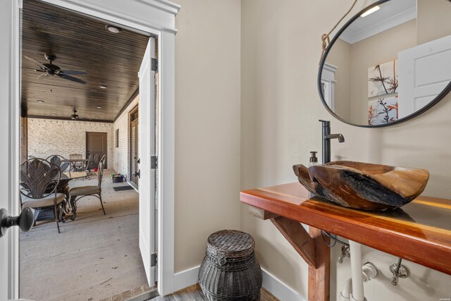 interior space with ceiling fan, brick wall, a sink, baseboards, and crown molding