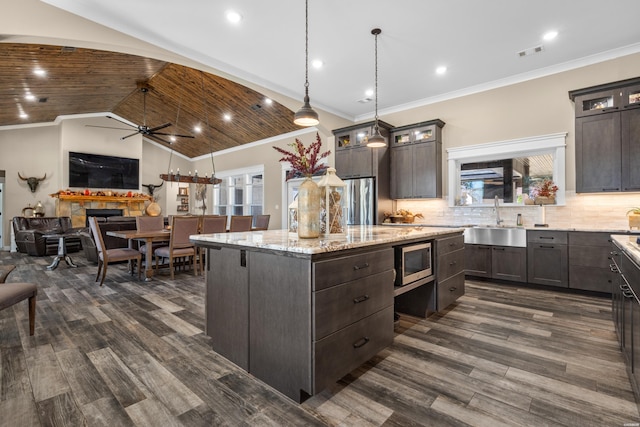 kitchen featuring appliances with stainless steel finishes, glass insert cabinets, a sink, and a center island