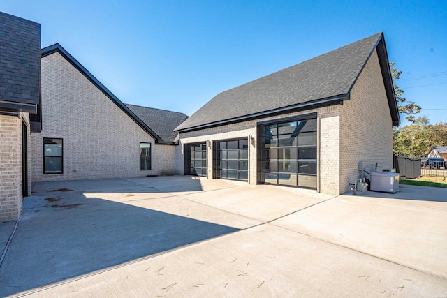 rear view of property featuring a patio area, roof with shingles, and brick siding