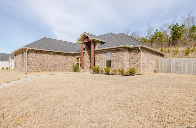 view of front of house with brick siding, fence, and roof with shingles