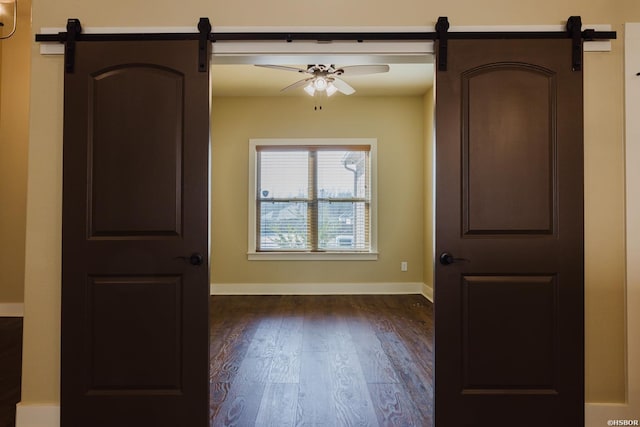 unfurnished room with ceiling fan, a barn door, dark wood-type flooring, and baseboards