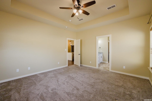 unfurnished bedroom featuring carpet floors, visible vents, a tray ceiling, and baseboards