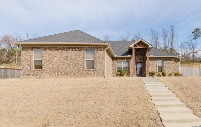 view of front facade with roof with shingles, fence, and brick siding