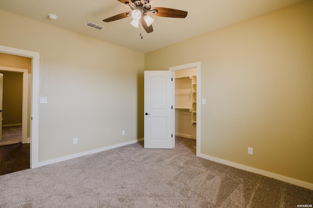 unfurnished bedroom with carpet floors, visible vents, a spacious closet, a ceiling fan, and baseboards