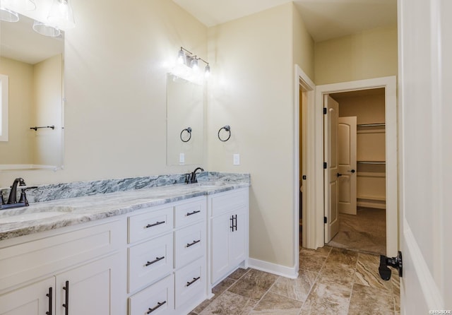 full bathroom featuring a walk in closet, a sink, baseboards, and double vanity