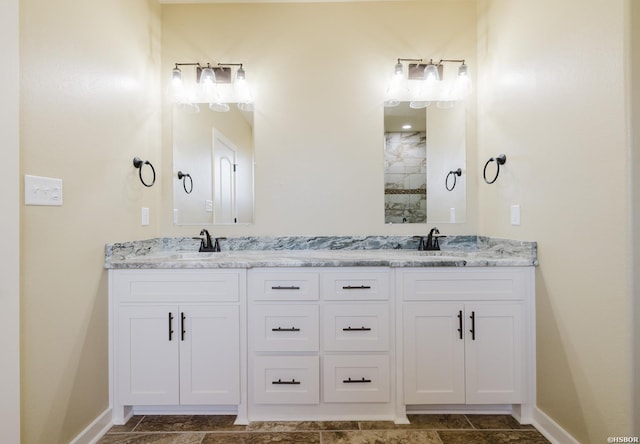 bathroom with double vanity, tiled shower, a sink, and baseboards